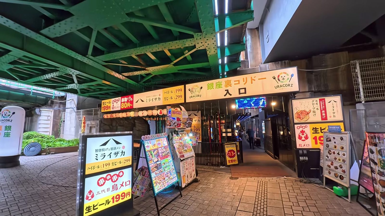 新橋の高架下。緑の鉄骨の下に、銀座裏コリドーの入口と飲食店の看板